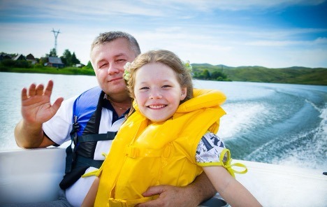 Father and daughter smiling on boat wearing life jackets 